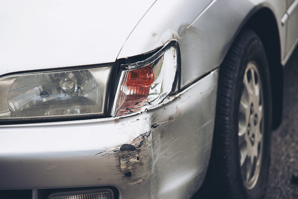 Close-up of a car’s front corner showing scratches, dents, and damage