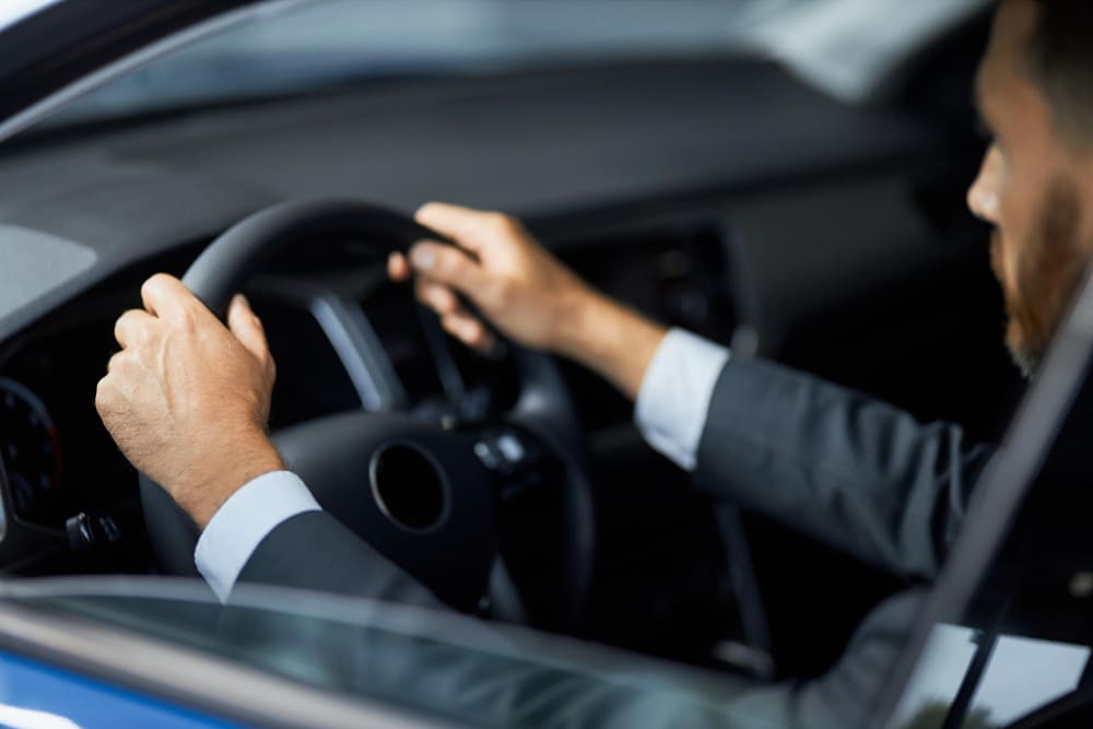 Person in a suit sitting in a car, gripping the steering wheel with one hand