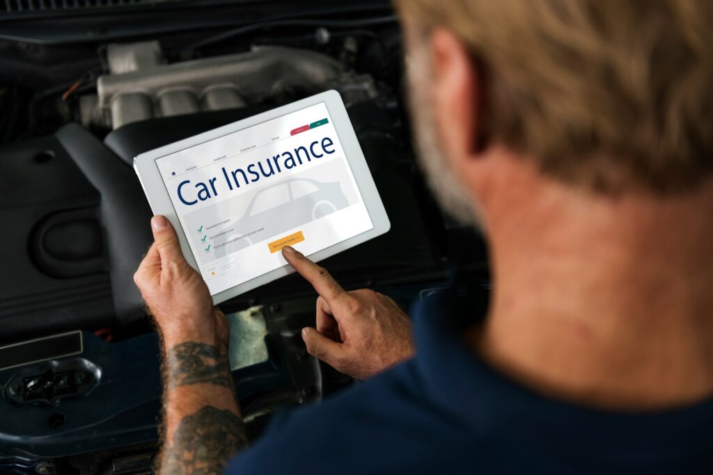 Mechanic or car owner browsing a car insurance website on a tablet over an open car hood
