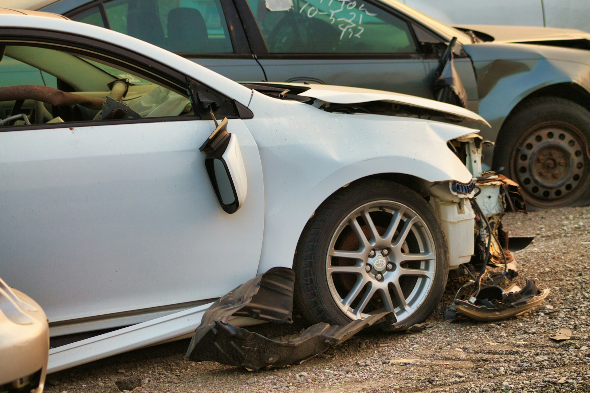 Severely damaged white car with crushed front end in a salvage yard after a collision
